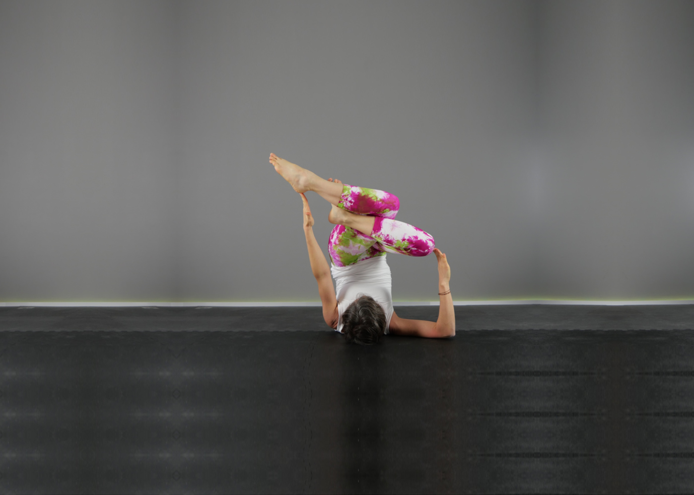 Elisabetta Baso insegnante di vinyasa yoga a padova esegue un’asana, posizione yoga, variante di Sarvangasana, la posizione della candela, con le gambe accavallate con in Garudasana, la posizione dell’aquila un braccio disteso perpendicolare verso l’alto e l’altro piegato verso l’alto ad angolo retto