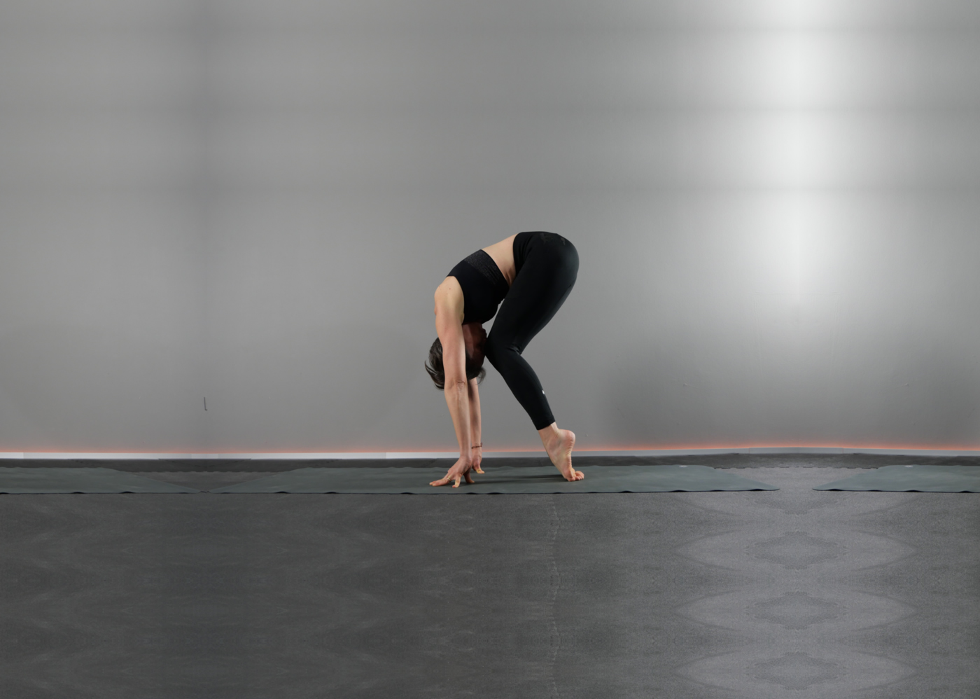 Elisabetta Baso durante la sua lezione di yoga a padova esegue un’asana, posizione yoga, variante di Uttanasana, la posizione della pinza in piedi, con le ginocchia leggermente piegate, il dorso dei piedi a terra, i polpastrelli delle mani appoggiati a terra, le braccia distese perpendicolari al pavimento, la schiena curva e il viso tocca le ginocchia